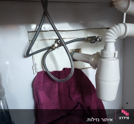 צנרת מתחת לכיור עם מגבת סגולה